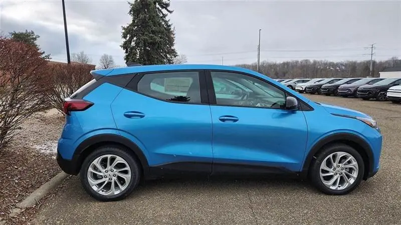 A blue 2027 Chevrolet Bolt seen from the passenger side in a vehicle storage lot in Novi, Michigan