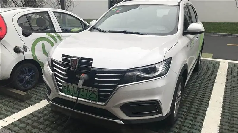 A white Roewe electric SUV with a green Shanghai license plate charging at a public charging bay