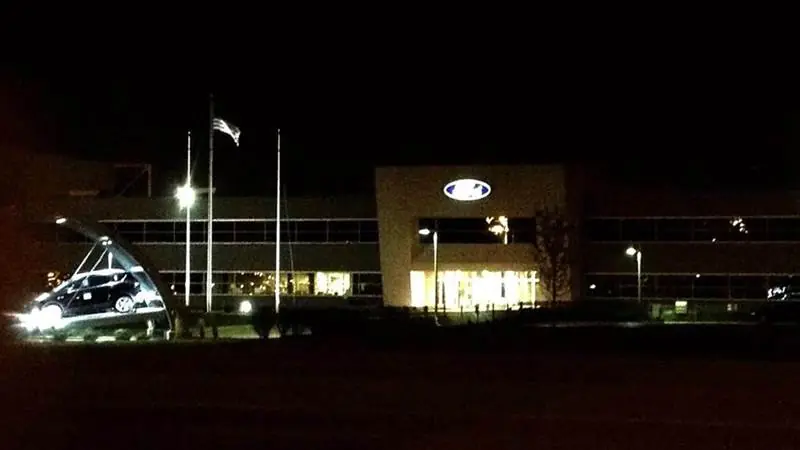 The illuminated Ford logo glowing above the main entrance of Louisville Assembly Plant at night, the factory chosen to build Ford's new affordable electric pickup