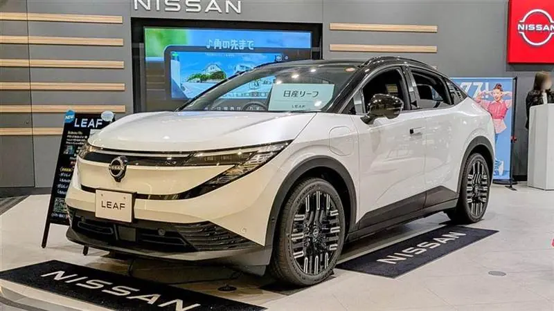 A white third-generation Nissan Leaf on display in a Nissan dealership showroom, with LEAF branding and the Nissan logo visible behind it