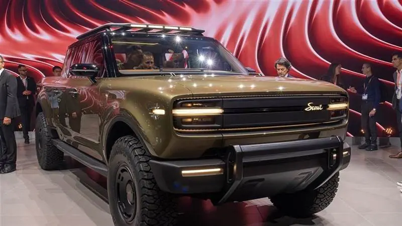 The new electric Scout Terra pickup on public display at IAA Mobility 2025 in Munich, its illuminated Scout grille lettering visible as show visitors look on
