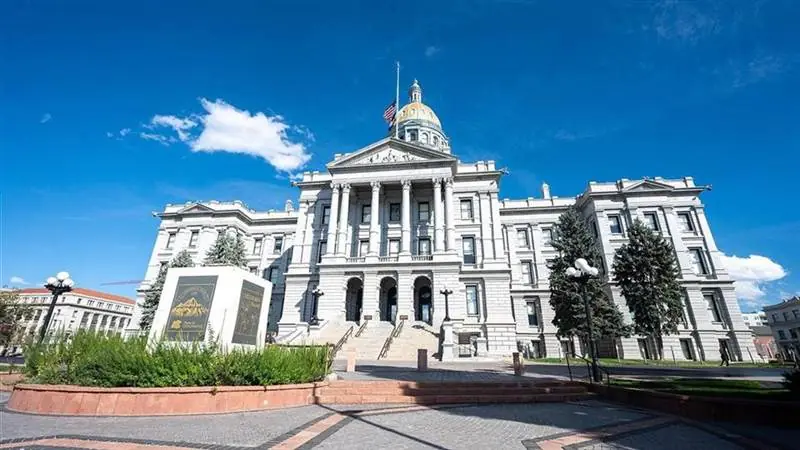 The Colorado State Capitol in Denver, a white granite building with a gold dome flying the American flag under a blue sky