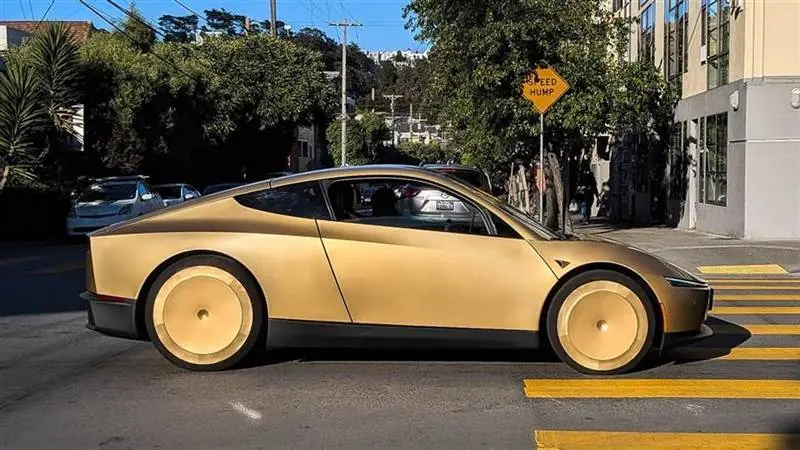 A gold Tesla Cybercab with butterfly doors parked on a sunny San Francisco street, shown in side profile with its covered rear wheels visible