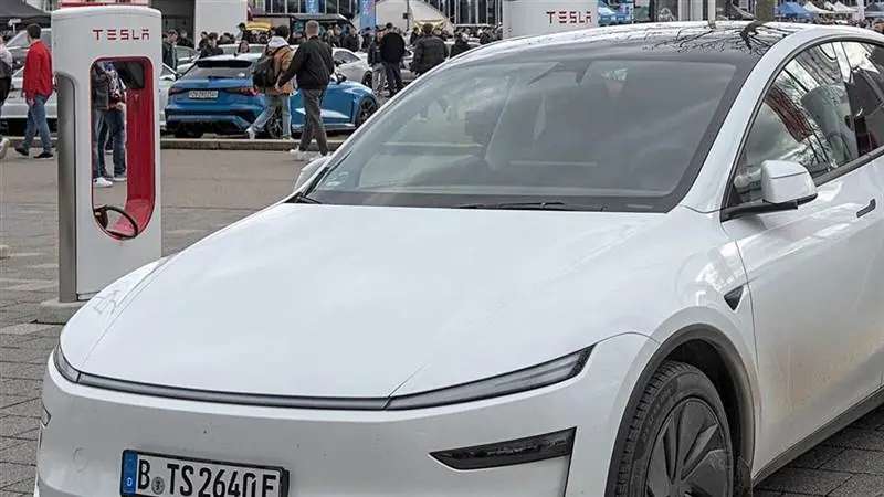 White Tesla Model Y parked beside a red-and-white Tesla Supercharger charging post