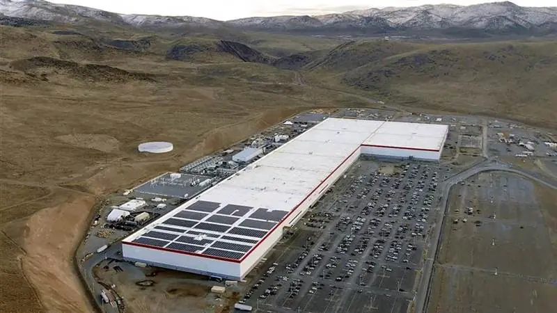 Aerial view of the Tesla Gigafactory battery plant near Sparks, Nevada, a long white factory building with solar panels on its roof beside a full parking lot