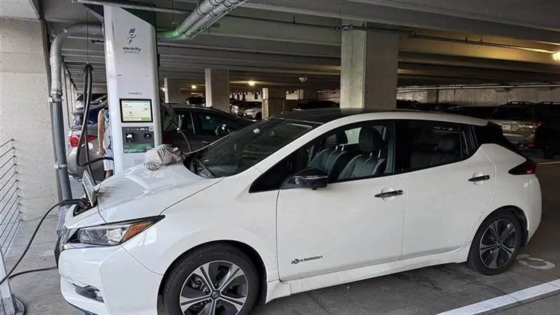 A white Nissan Leaf charging at an Electrify America station in a parking garage in Somerville, Massachusetts